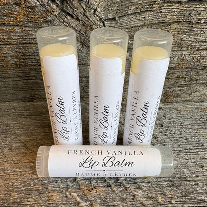 Four tubes of French Vanilla Lip Balm arranged on a rustic weathered wood surface, with three standing upright and one lying horizontally in front.