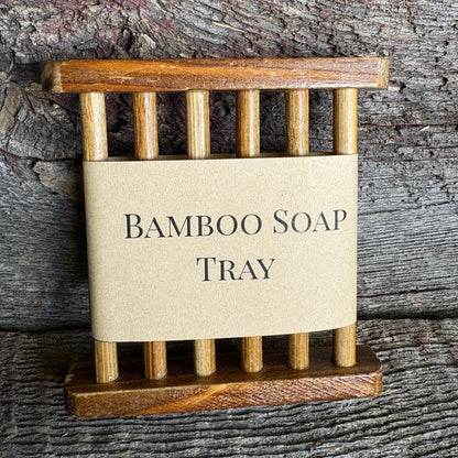 A small bamboo soap tray with a natural kraft paper label reading 'BAMBOO SOAP TRAY' in black serif text, photographed against a rustic weathered wood background.