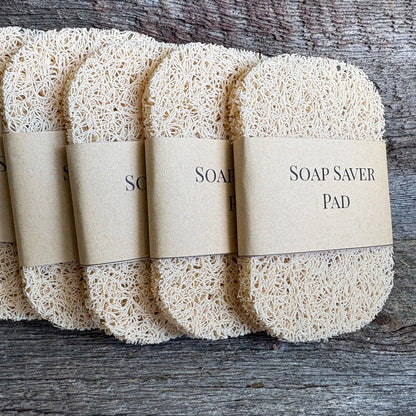 Five synthetic loofah soap saver pads wrapped in kraft paper bands, arranged in a fan on a rustic weathered wood background.